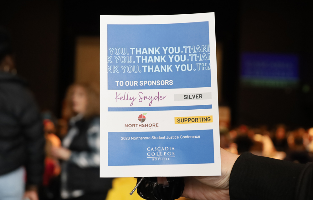 Fitness Center Sign in focus that reads, 'Thank you. Thank you. Thank you. To our sponsors Kelly Snyder, silver; Northshore Schools Foundation, supporting; 2023 Northshore Student Justice Conference' and Cascadia logo in front of an out of focus banquet crowd